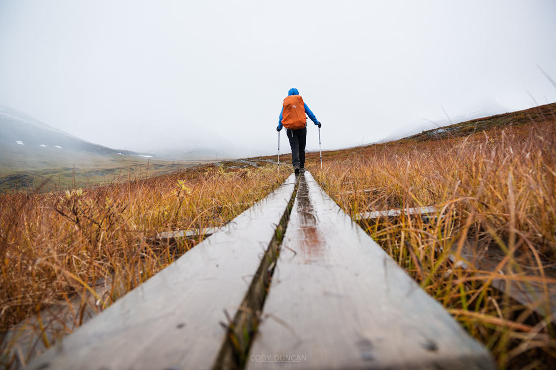 Female hiker walks along wooden planks in Tjäktjavagge on Kungsleden trail, Lappland, Sweden