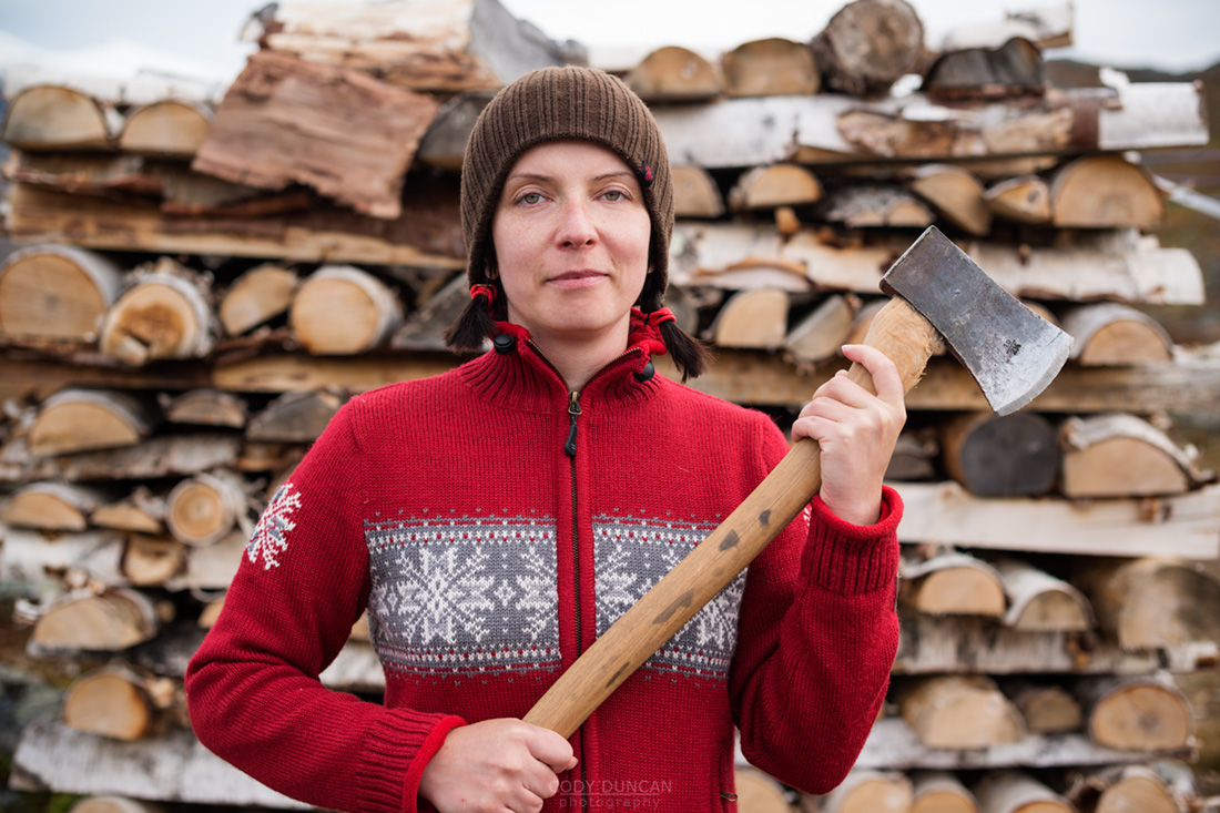 Female hiker in nordic style sweater holding axe to cut firewood at mountain hut, Kungsleden trail, Lappland, Sweden
