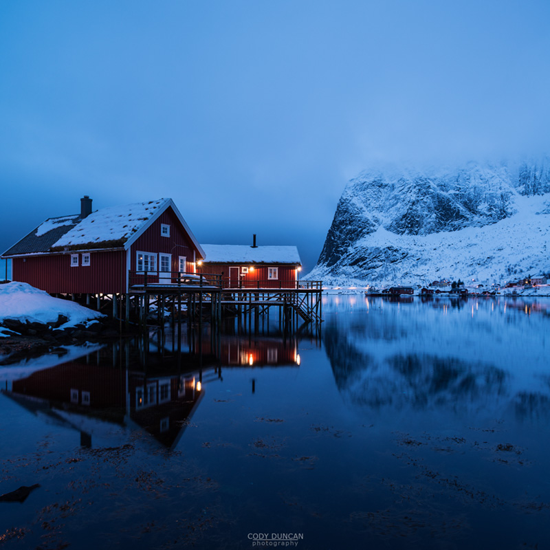 Traditional Rorbu cabin reflects in fjord in evening light, Valen, Reine, Moskenesøy, Lofoten Islands, Norway