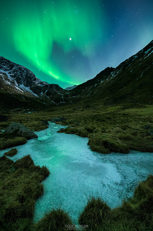 Northern Lights - Aurora Borealis shine in sky over frozen ice river and mountain landscape, Flakstadøy, Lofoten Islands, Norway