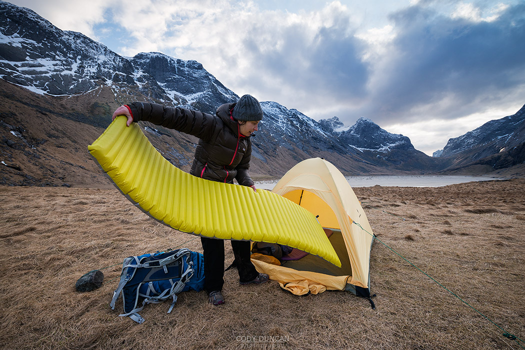 Female hiker sets up tent on wild camping trip to Horseid beach, Moskenesøy, Lofoten Islands, Norway