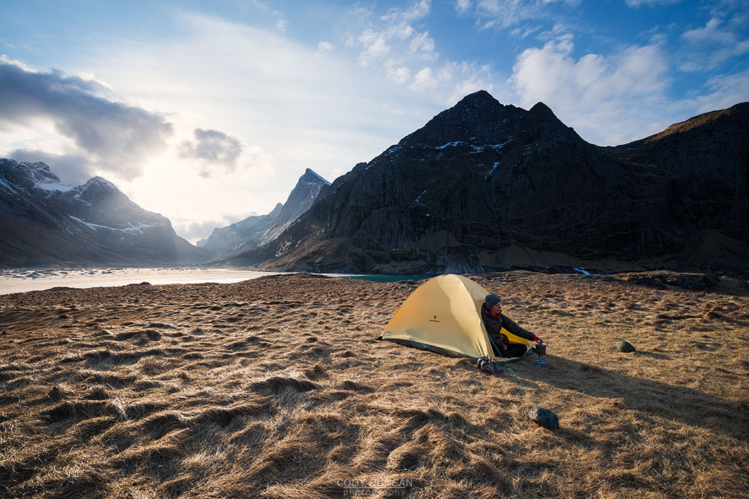 Female backpacker takes in view from tent while camping at Horseid beach, Moskenesøy, Lofoten Islands, Norway