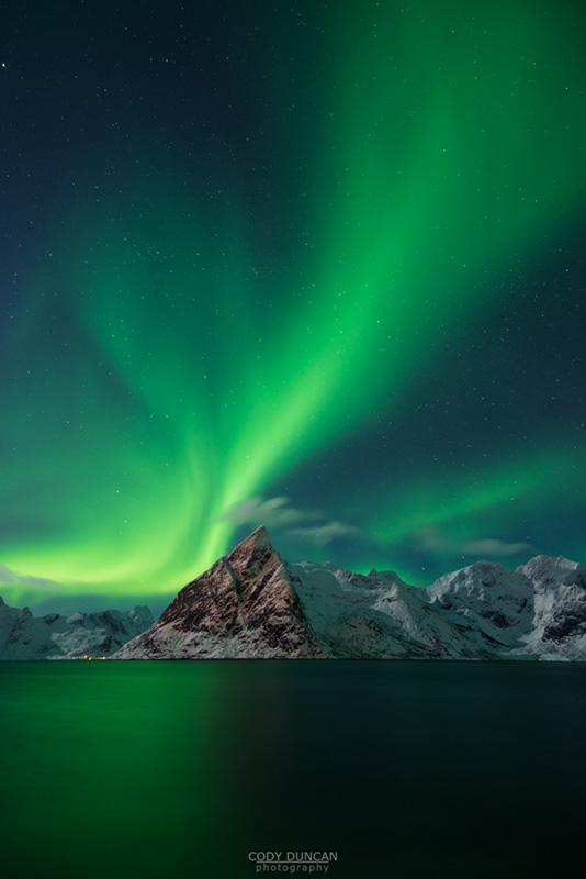 Aurora Borealis - Northern Lights fill sky over Olstind mountain peak and reflect in fjord, Toppøya, Lofoten Islands, Norway